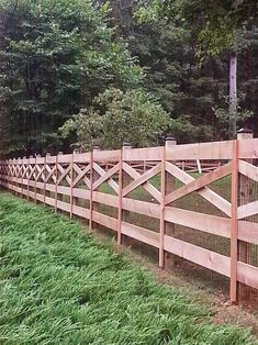 a wooden fence in the middle of a grassy area with trees and bushes behind it