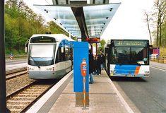 two public transit buses stopped at a train station with passengers waiting for the next train