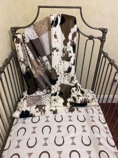 a baby crib with a cow print blanket on it's side and several blankets folded up in the middle