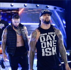 two men standing next to each other in front of a stage with one man wearing a hat