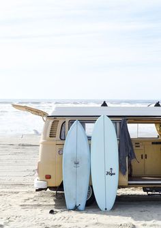 two surfboards are propped up in front of an old vw van on the beach