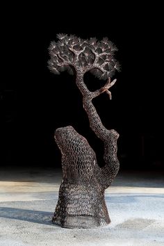 a metal tree sculpture sitting on top of a cement floor next to a black wall