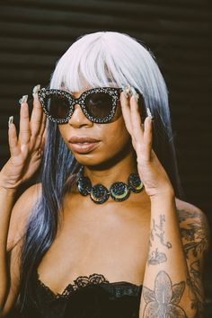 a woman with white hair wearing sunglasses and holding her hands up to her face while looking at the camera