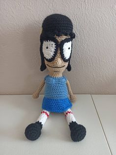 a crocheted doll wearing glasses and a blue dress is sitting on a table