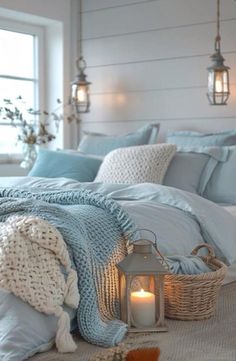 a bed with blue blankets and pillows next to a candle in a basket on the floor