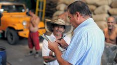 a man writing on a clipboard while other men stand in the background with trucks behind him