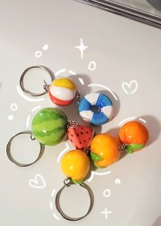 a bunch of fruit key chains are on a table with some watermelon, oranges and other fruits