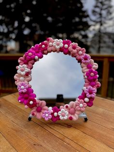 a pink and white flowered mirror sitting on top of a wooden table