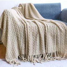 a couch with a blanket on top of it next to a blue chair and white wall