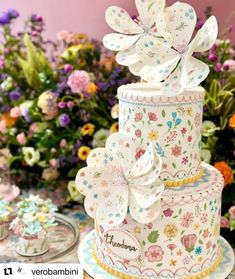 there is a three tiered cake with flowers on the top and bottom, sitting in front of colorful flowers