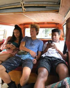 four people sitting in the back of a van looking at their cell phones and taking pictures