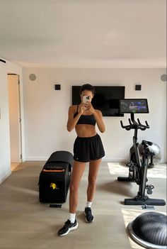 a woman taking a selfie in front of an exercise bike and treadmills