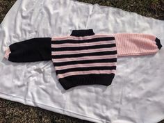 a black and pink sweater laying on top of a white sheet with grass in the background