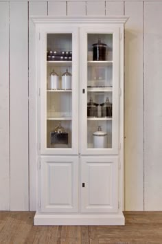 a white china cabinet with glass doors on the top and bottom shelves, in front of a wooden floor