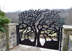 an iron gate with a tree design on the top and bottom, in front of a stone wall