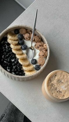 a bowl of cereal with bananas and blueberries next to a cup of coffee on a table