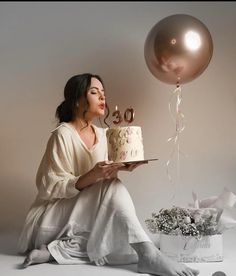 a woman sitting on the floor with a cake and balloons in front of her,