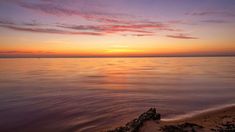 the sun is setting over the water at the beach with rocks in the foreground