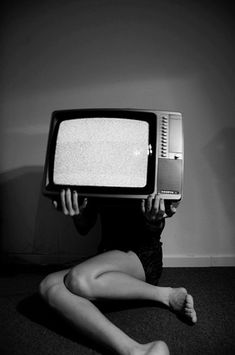 a woman sitting on the floor holding up an old tv