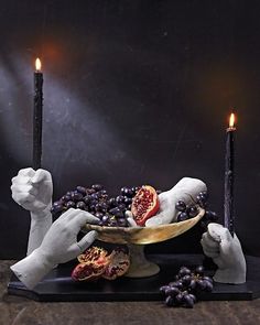 two candles are lit in the shape of hands holding a bowl with grapes on it