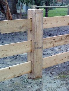 a wooden fence in the middle of a dirt field with trees and grass behind it