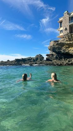 two people swimming in the ocean near a building