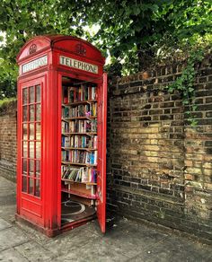 a red phone booth sitting next to a brick wall with bookshelves in it