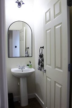 a white sink sitting under a bathroom mirror next to a doorway with an open door