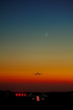 an airplane is flying in the sky at sunset or dawn with a crescent moon behind it