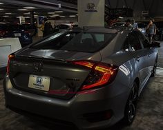 the back end of a gray car parked in a garage with people looking at it