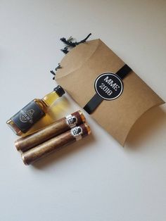 three cigars and two bottles of liquor sitting on a white counter top next to a brown paper bag