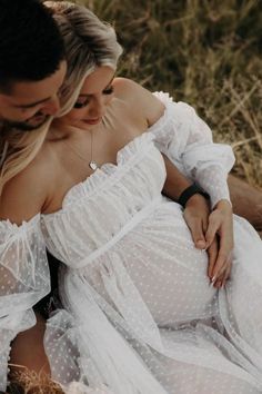 a man and woman are sitting on the ground in white dresses looking at each other