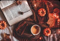 an open book, cup of coffee and some pumpkins on a table with lights