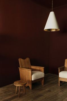 two chairs and a foot stool in a room with red walls, wooden flooring and a lamp hanging from the ceiling