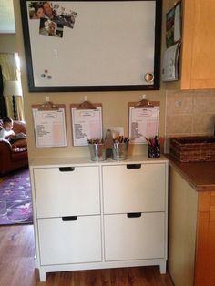 there is a white cabinet in the kitchen with two cups on it and three clipboards attached to the wall