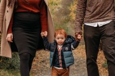 a man and woman holding hands while walking with a small child on a path in the woods