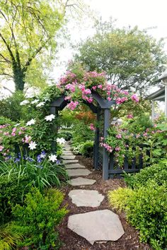 a garden with pink and white flowers growing on it's sides, surrounded by greenery