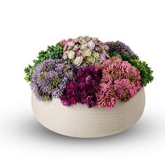 a white bowl filled with lots of purple and green flowers on top of a table