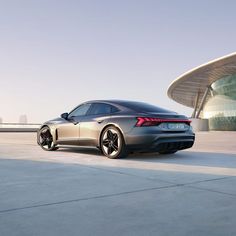 a silver sports car parked in front of a building with a large circular structure behind it