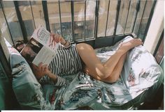 a woman laying in bed reading a book with her legs crossed and head on the pillow