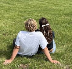 two people sitting in the grass looking at an airplane