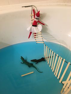 an elf is in the bathtub playing with sticks and toothpicks while another toy lies on the floor