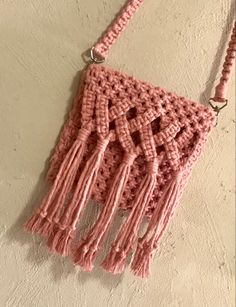 a pink crocheted purse hanging on the wall with tassels attached to it