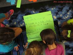 three children sitting at a table writing on a piece of paper with sticky notes attached to it