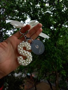 a hand holding a keychain with a white ribbon attached to it and a name tag