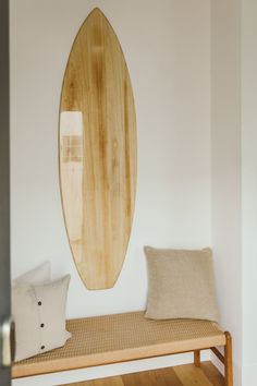 a wooden surfboard hanging on the wall above a bench with two pillows and a pillow