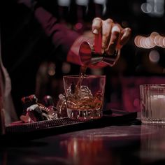 a person pouring drinks into glasses on a table with lights in the backgroud