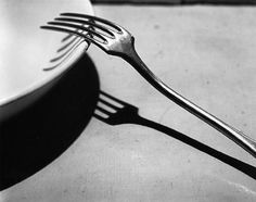 a black and white photo of a fork on a plate with the shadow of it