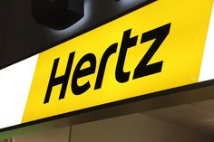 a yellow and black sign that says hertz next to a light on the wall