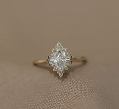 an engagement ring with a pear shaped diamond in the center on a beige cloth background